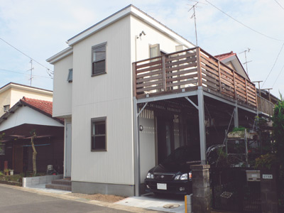 モダンなデザインの白い建物と、カースペースの上の大きなウッドデッキが特徴の栗原さんのお宅