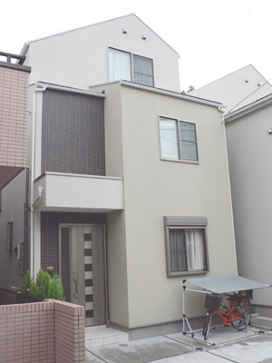 オフホワイトとベージュの壁にダークグレーのタイルのアクセントが利いたスタイリッシュな外観